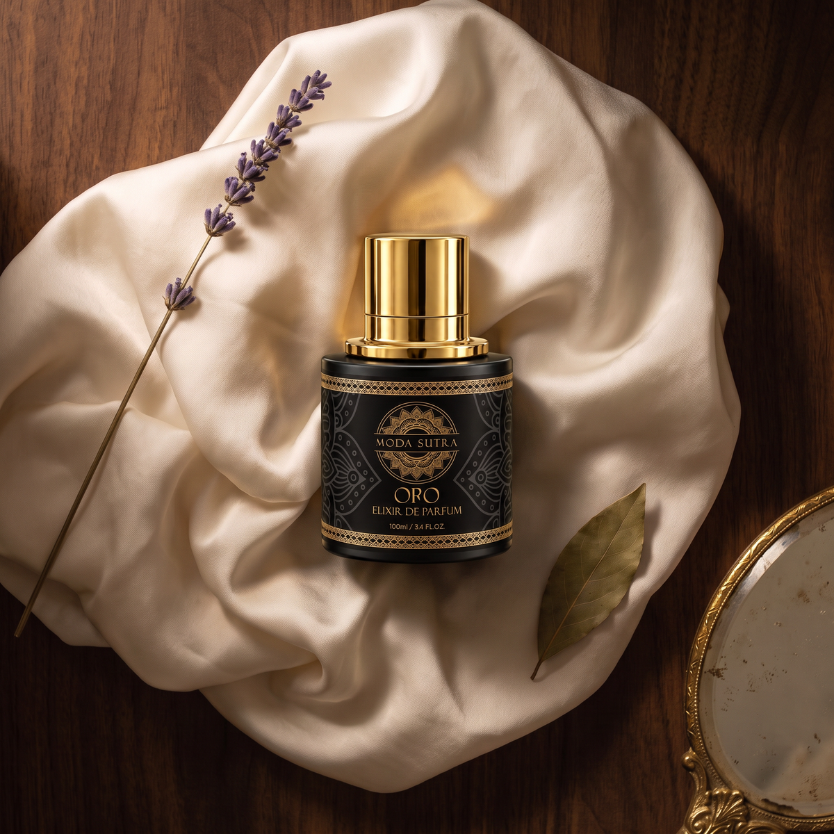 Moda Sutra Oro Elixir de Parfum flat-lay on ivory silk with dried florals and antique gold accents — 100 mL matte-black flacon, gold-foil mandala label.