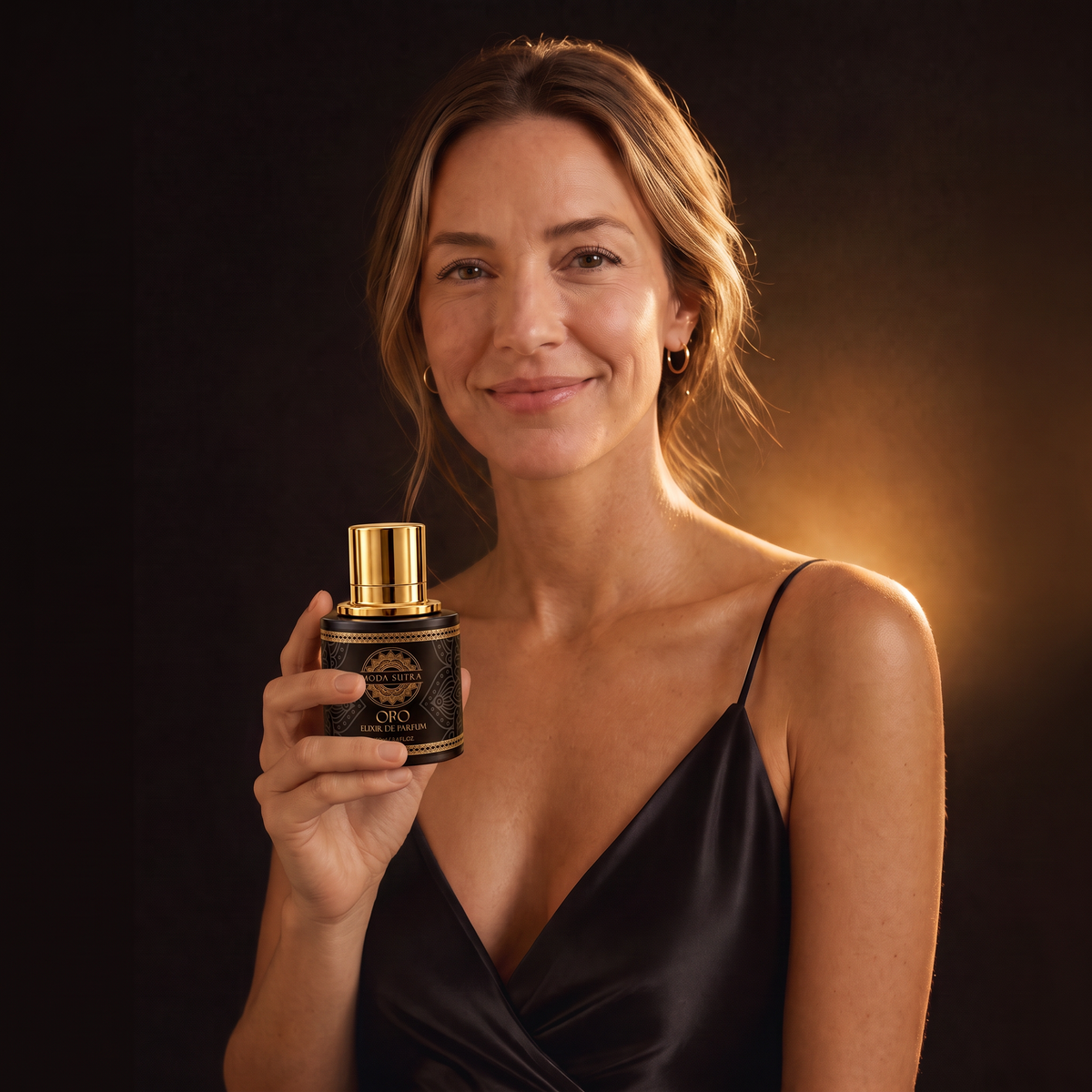 Blonde woman in silk holding a Moda Sutra Oro Elixir de Parfum bottle — editorial fragrance photograph, warm gold light, Miami clean-luxury brand.