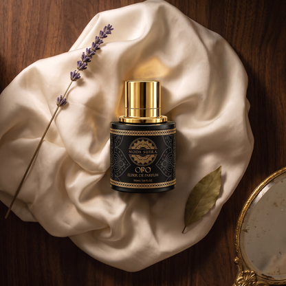 Moda Sutra Oro Elixir de Parfum flat-lay on ivory silk with dried florals and antique gold accents — 100 mL matte-black flacon, gold-foil mandala label.